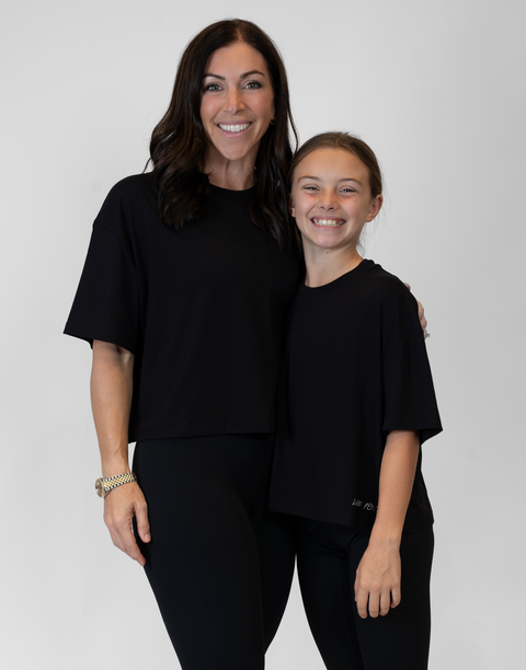 Woman and girl standing together wearing ladies Bamboo Mid-Crop Tee with "Luke 18:1" text above bottom seam
