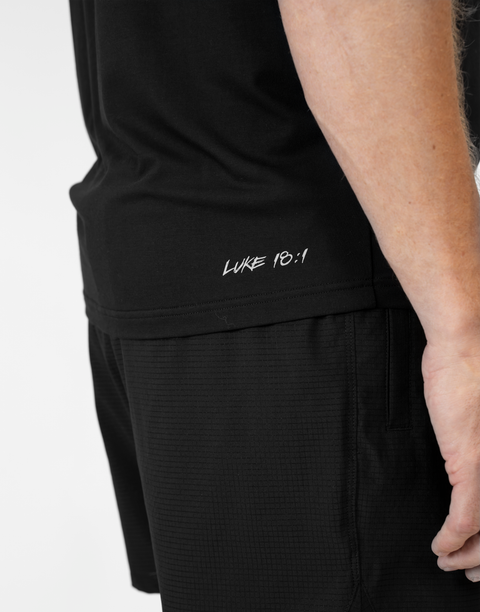 Rear view of man wearing Men's black Bamboo Performance Tee showing "LUKE 18:1" text on right back side near the bottom seam