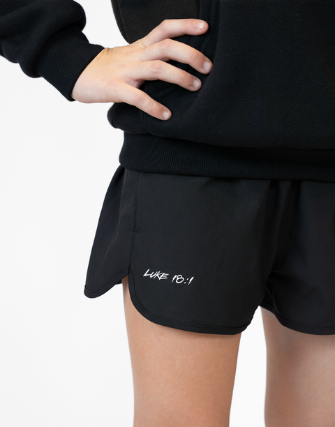 Girl wearing girls black flowy performance short with "LUKE 18:1" text