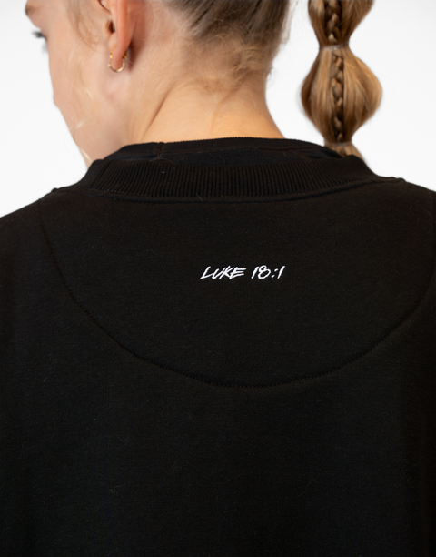 rear view of girl wearing Ladies Black Relaxed Fleece Crew with "LUKE 18:1" text on upper back