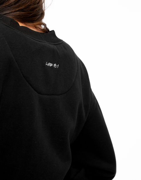 Rear view of woman wearing Ladies Black Relaxed Fleece Crew with "LUKE 18:1" text on back