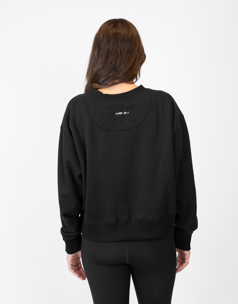 Rear view of woman wearing Ladies Black Relaxed Fleece Crew with "LUKE 18:1" text on back