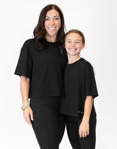 Woman and girl standing together wearing ladies Bamboo Mid-Crop Tee with "Luke 18:1" text above bottom seam