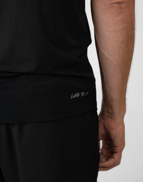 Rear view of man wearing Men's black Bamboo Performance Tee showing "LUKE 18:1" text on right back side near the bottom seam