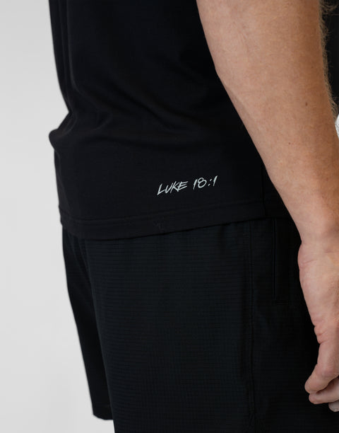 Rear view of man wearing Men's black Bamboo Performance Tee showing "LUKE 18:1" text on right back side near the bottom seam