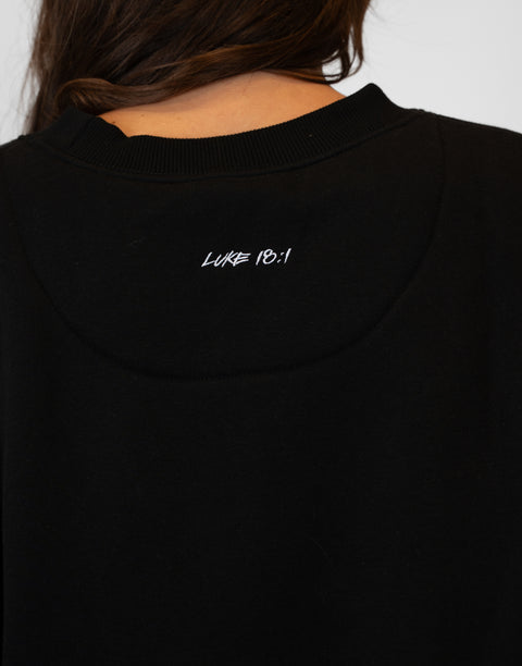 Rear view of woman wearing Ladies Black Relaxed Fleece Crew with "LUKE 18:1" text on back