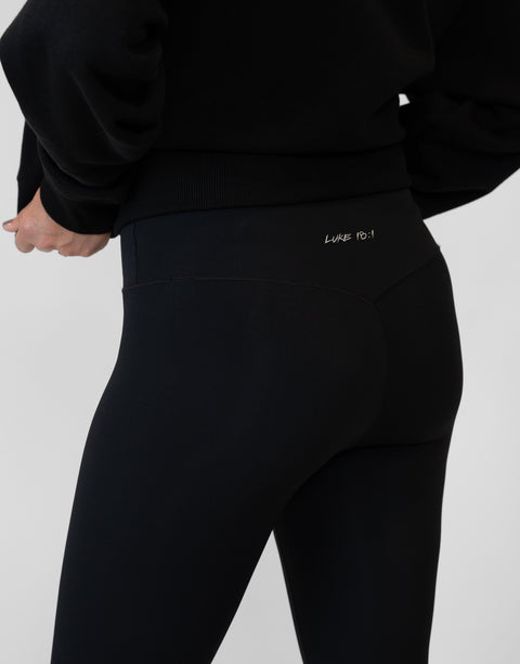 rear view of person wearing black Ladies Performance Legging with "LUKE 18:1" text on waistband