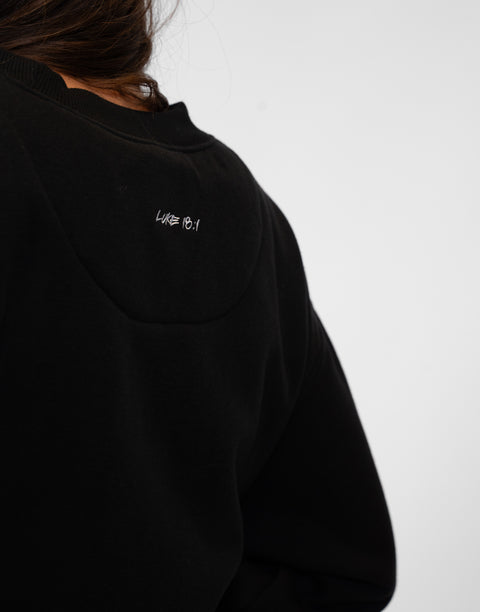 Rear view of woman wearing Ladies Black Relaxed Fleece Crew with "LUKE 18:1" text on back