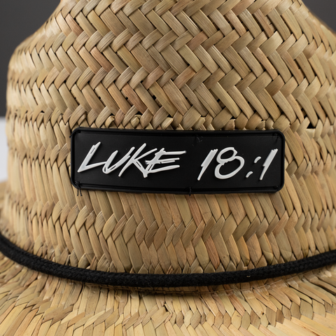 closeup of Straw hat with "LUKE 18:1" patch on front