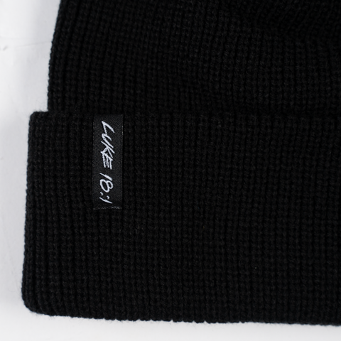 closeup of white "LUKE 18:1" label on black beanie