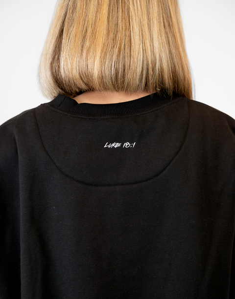 Rear view of woman wearing Ladies Black Relaxed Fleece Crew with "LUKE 18:1" text on back