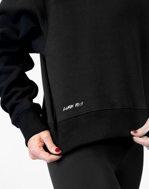 Woman wearing Ladies Black Relaxed Fleece Crew with "LUKE 18:1" text on lower side
