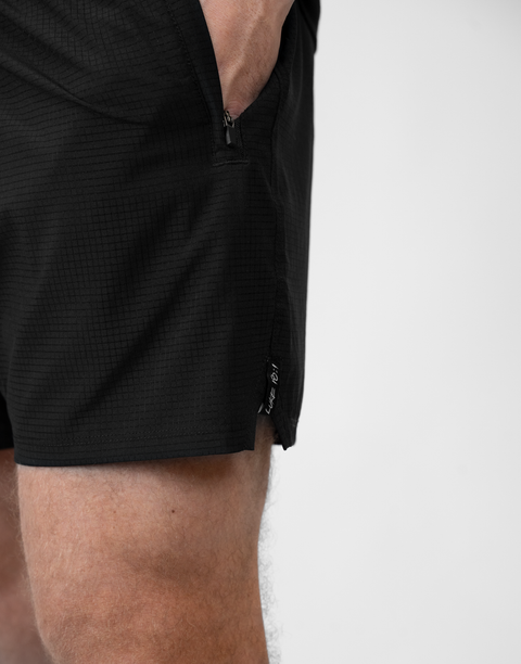 side view of man wearing Men's Black 6" Airflow Short showing "LUKE 18:1" text on side seam