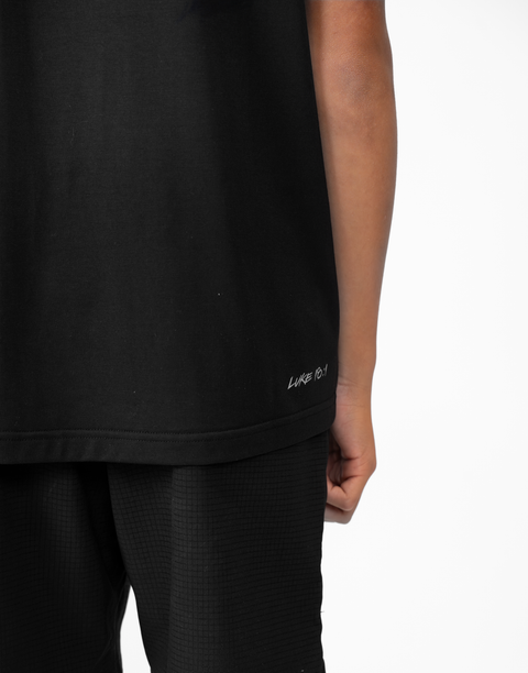 Rear view of boy wearing Youth black Bamboo Performance Tee with "LUKE 18:1" text on back above lower seam