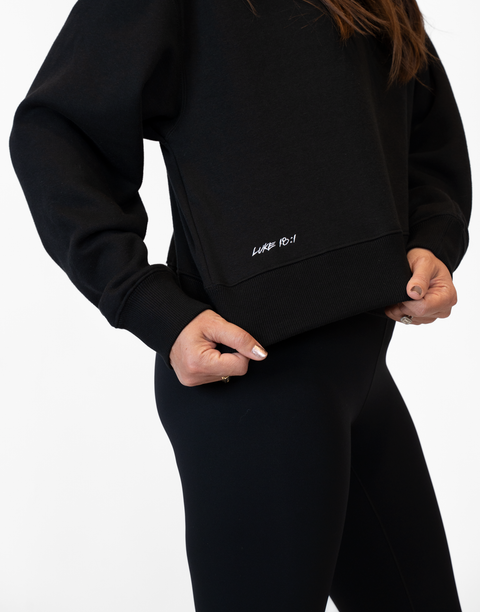 Person wearing Ladies Black Relaxed Fleece Crew with "LUKE 18:1" text on lower side