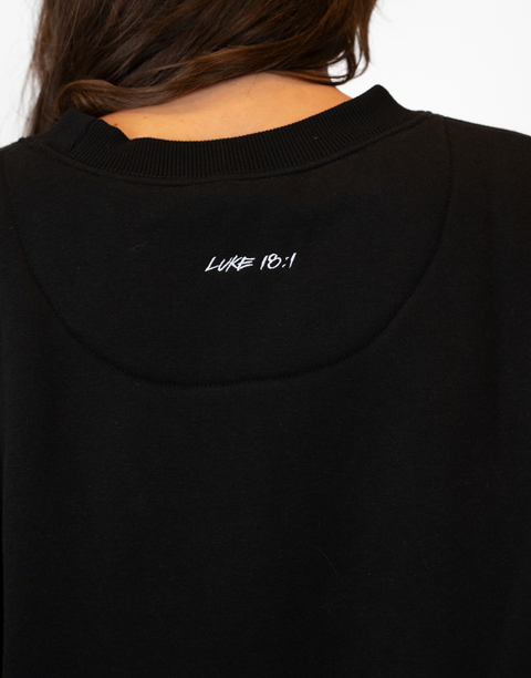 Rear view of woman wearing Ladies Black Relaxed Fleece Crew with "LUKE 18:1" text on back