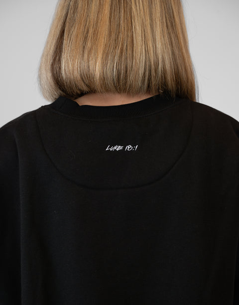 Rear view of woman wearing Ladies Black Relaxed Fleece Crew with "LUKE 18:1" text on back