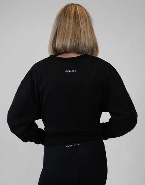 Rear view of woman wearing Ladies Black Relaxed Fleece Crew with "LUKE 18:1" text on back