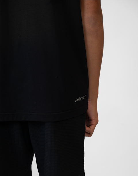 Rear view of boy wearing Youth black Bamboo Performance Tee with "LUKE 18:1" text on back above lower seam