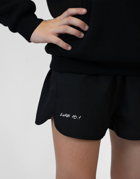 Girl wearing girls black flowy performance short with "LUKE 18:1" text