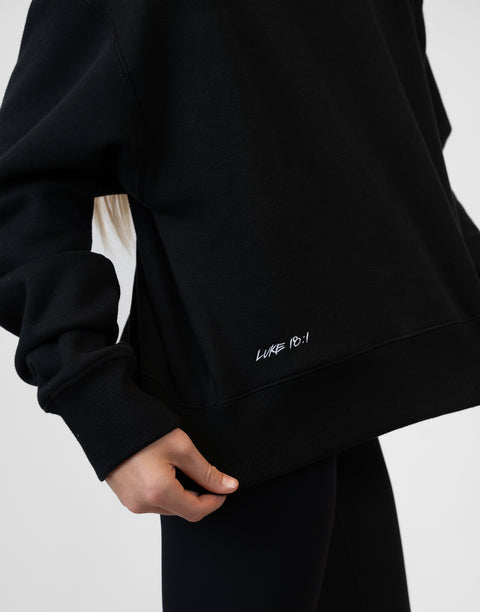 Person wearing Ladies Black Relaxed Fleece Crew with "LUKE 18:1" text on lower side