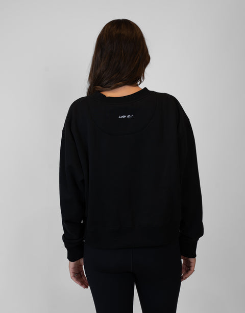 Rear view of woman wearing Ladies Black Relaxed Fleece Crew with "LUKE 18:1" text on back